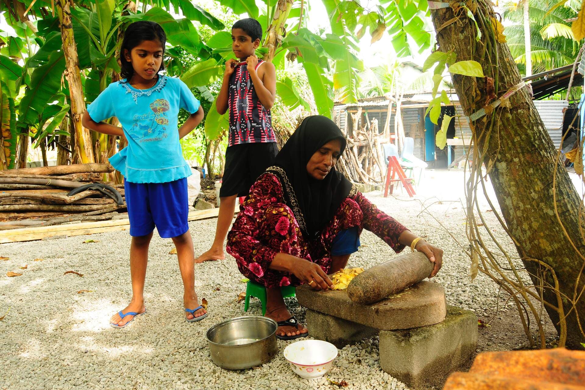 WHO Maldives / Ibrahim Asad A mother is using traditional Maldivian cooking utensils to prepare a meal for her children. Credits